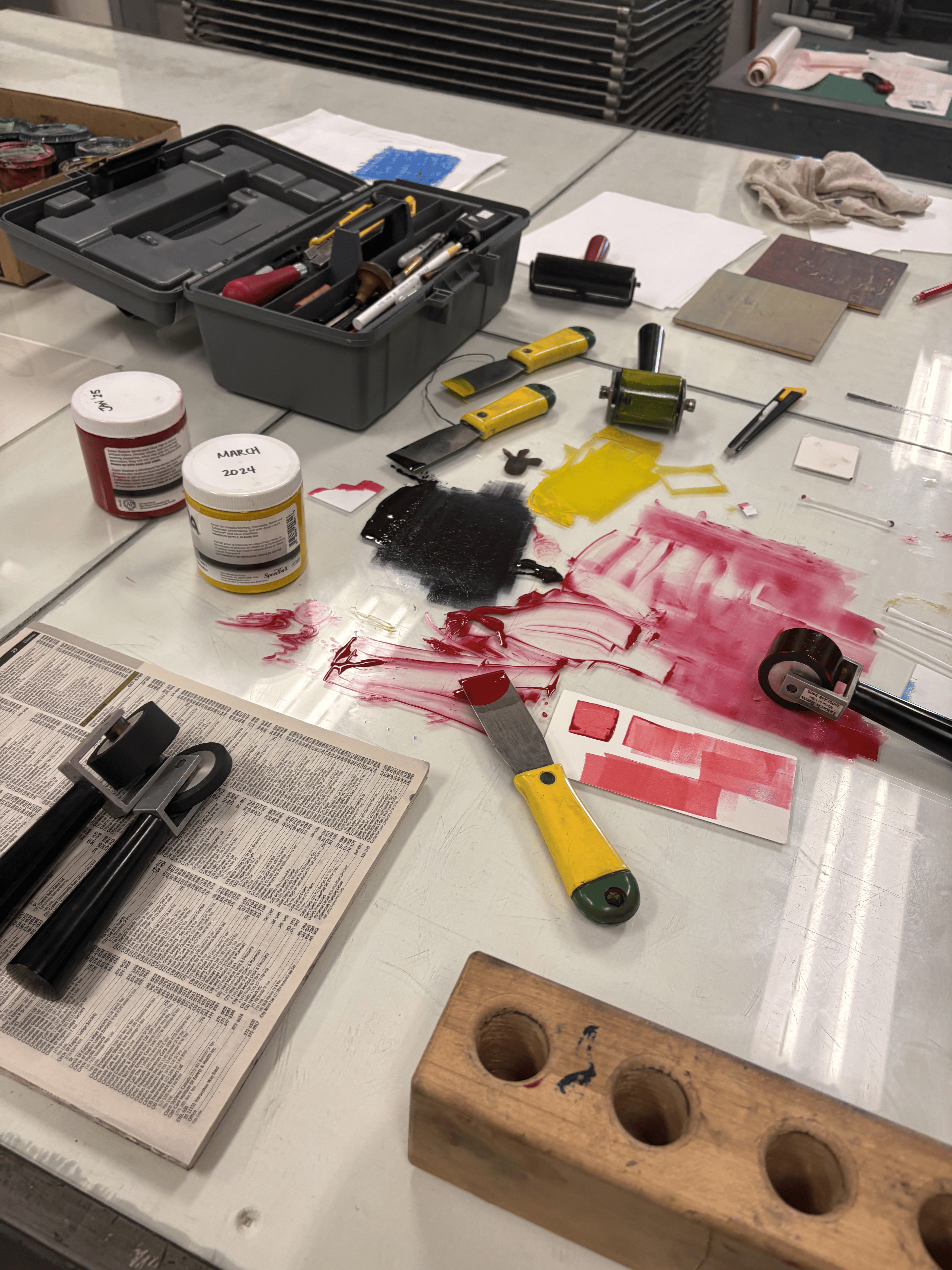 multiple materials used to create custom rubber stamps, objects include, rubber, carving tools, paint rollers, metal ink spatulas, coloured ink, made in the craft and design program at sheridan